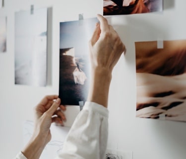 A womans hands taking a picture off the wall that was held on by a piece of tape. The photo she is taking off is of an outdoor desert landscape.